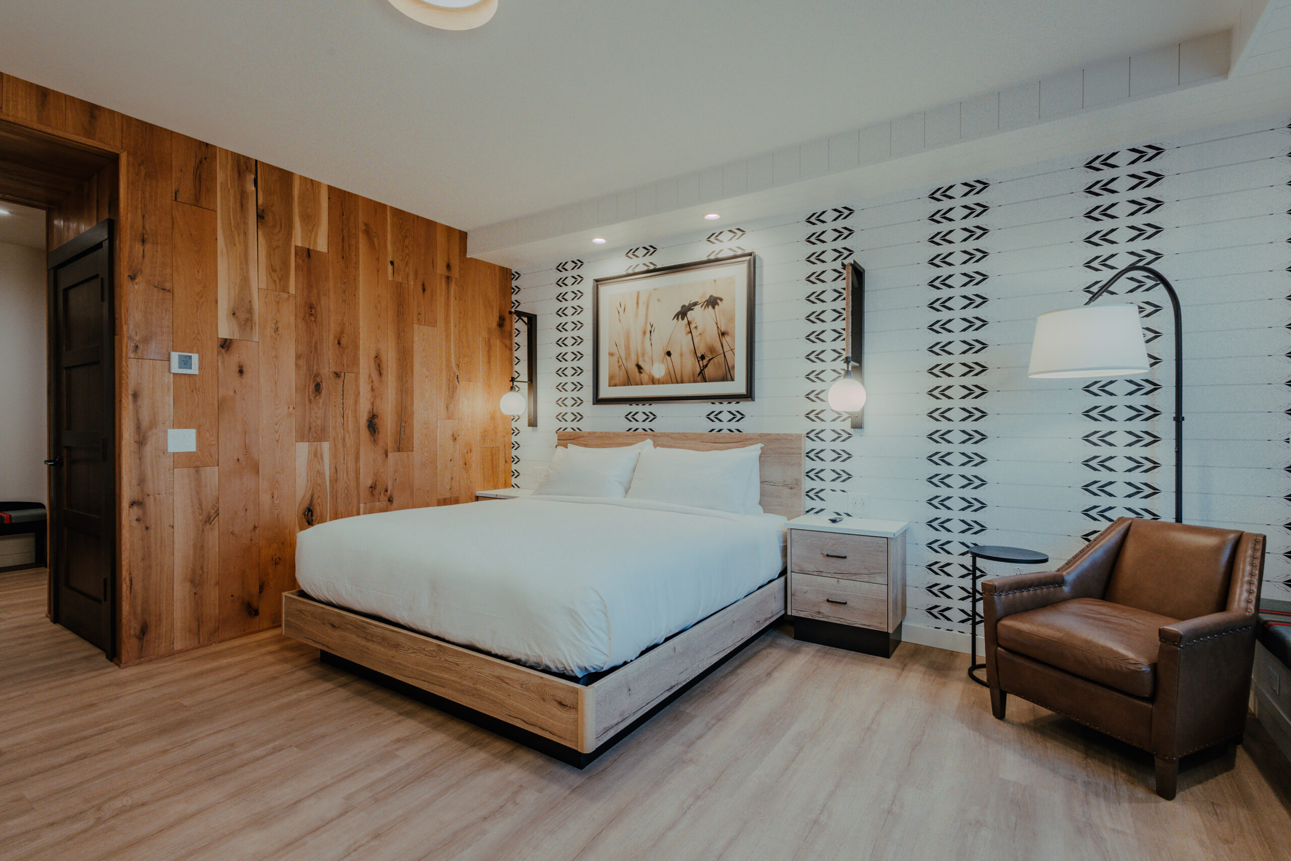 Corner King Room with king bed, wood accent wall, lounge chair, and patterned wall detail at Skaneateles Fields Resort & Spa.