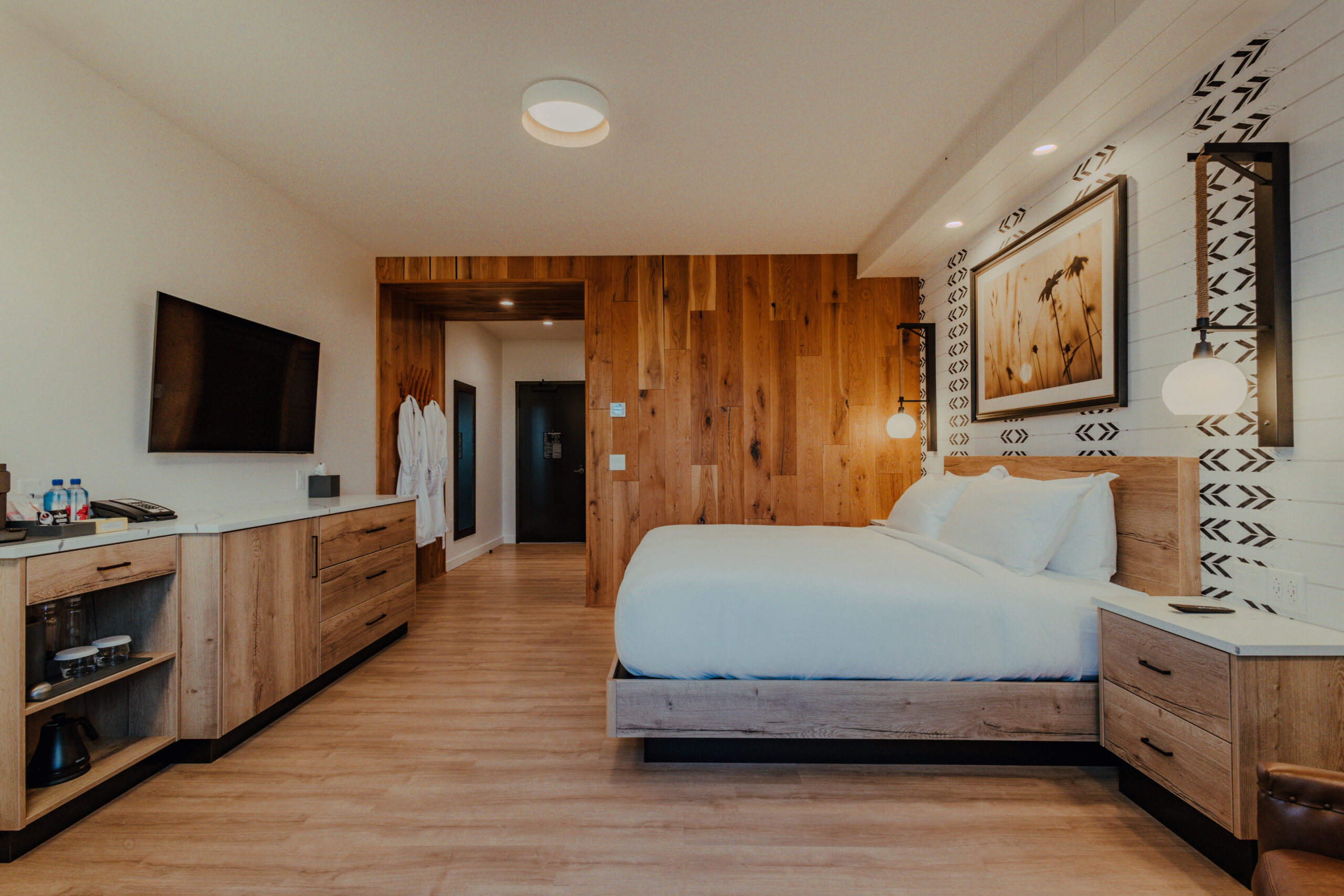King guest room with king bed, dresser, television, wood accents, and patterned wall detail at Skaneateles Fields Resort & Spa.