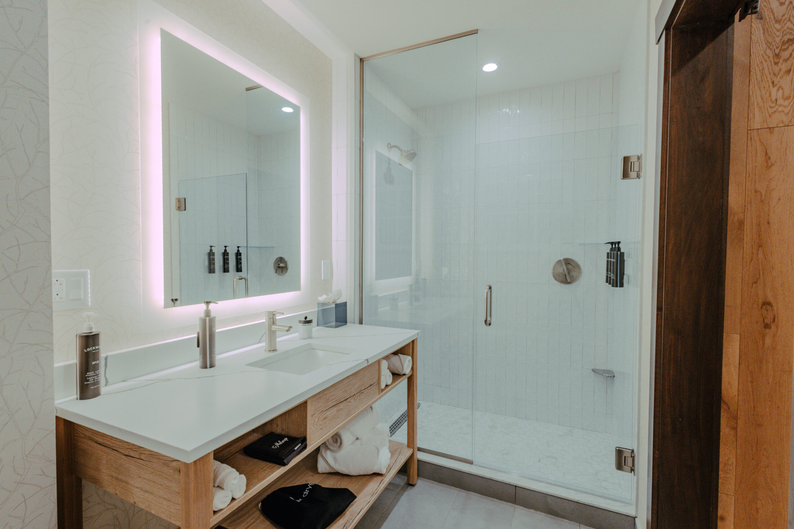 King Room bathroom with vanity, illuminated mirror, walk-in shower, and wood shelving at Skaneateles Fields Resort & Spa.