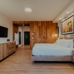 King guest room with king bed, dresser, television, wood accents, and patterned wall detail at Skaneateles Fields Resort & Spa.