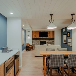 Lodge Suite dining area with table seating, kitchenette, wood cabinetry, and blue accent wall at Skaneateles Fields Resort & Spa.